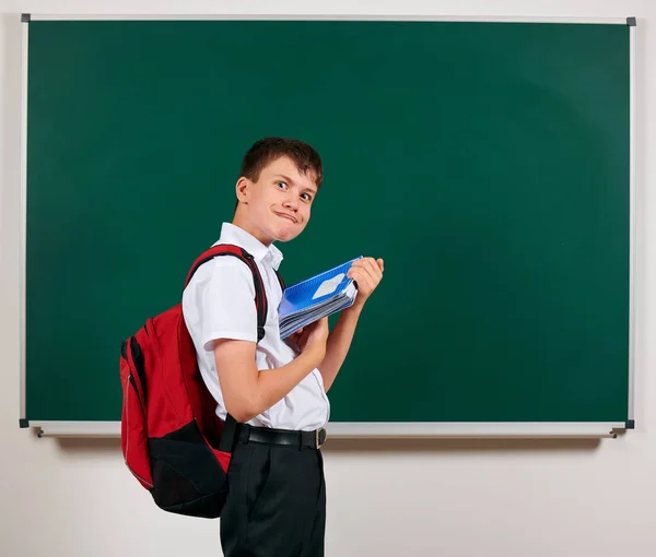 Retrato de un chico de escuela posando con mochila y útiles escolares, fondo de pizarra - vuelta a la escuela y concepto de educación — Foto de Stock