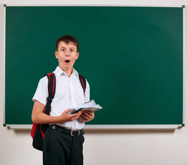 Porträt eines Schuljungen, der mit Rucksack und Schulmaterial posiert, Tafel-Hintergrund - zurück zu Schule und Bildungskonzept — Stockfoto