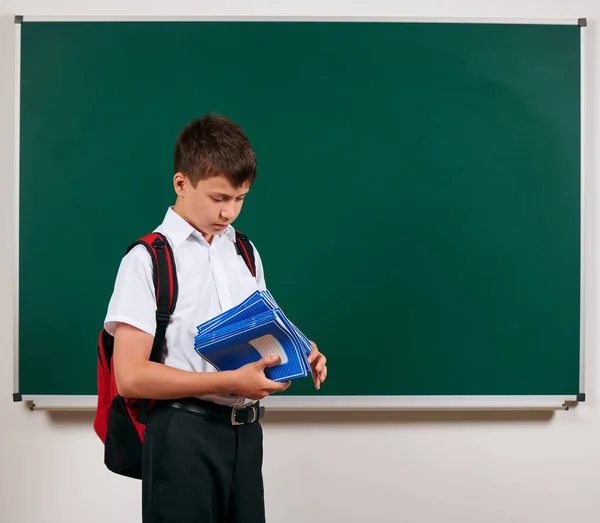 Porträt eines Schuljungen, der mit Rucksack und Schulmaterial posiert, Tafel-Hintergrund - zurück zu Schule und Bildungskonzept — Stockfoto