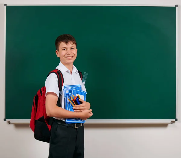 Retrato de um menino da escola posando com mochila e material escolar, fundo de quadro-negro - de volta ao conceito de escola e educação — Fotografia de Stock