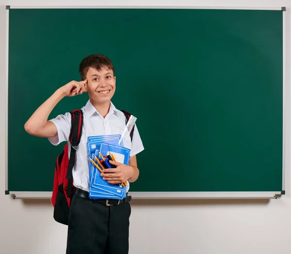 一个小学生摆姿势与背包和学习用品，黑板背景的肖像 - 回到学校和教育的概念 — 图库照片