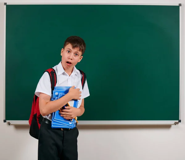 Ritratto di uno scolaro in posa con zaino e materiale scolastico, sfondo lavagna - ritorno a scuola e concetto di istruzione — Foto Stock