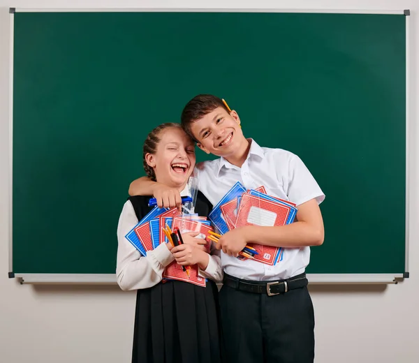 Portrait d'un écolier et d'une écolière posant avec des cahiers d'exercices, des stylos, des crayons et d'autres fournitures scolaires sur fond de tableau noir - concept de retour à l'école et d'éducation — Photo