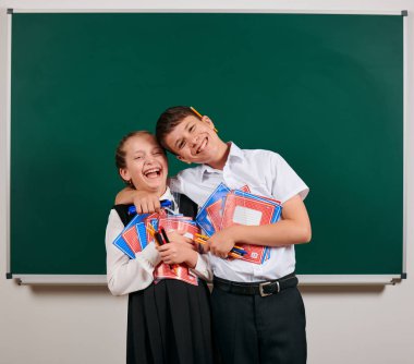 Bir okul çocuğu ve kız öğrenci nin duygusal portresi egzersiz kitapları, kalemler, kalemler ve kara tahta arka plan üzerinde diğer okul malzemeleri ile poz - geri okul ve eğitim kavramı