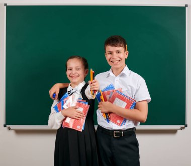 Bir okul çocuğu ve kız öğrenci nin duygusal portresi egzersiz kitapları, kalemler, kalemler ve kara tahta arka plan üzerinde diğer okul malzemeleri ile poz - geri okul ve eğitim kavramı
