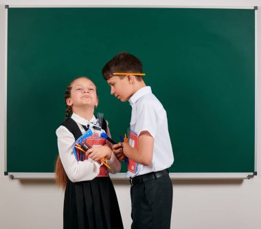 Bir okul çocuğu ve kız öğrenci nin duygusal portresi egzersiz kitapları, kalemler, kalemler ve kara tahta arka plan üzerinde diğer okul malzemeleri ile poz - geri okul ve eğitim kavramı