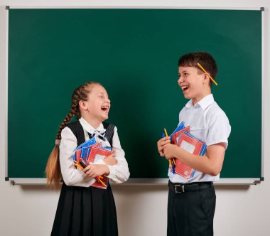 Bir okul çocuğu ve kız öğrenci nin duygusal portresi egzersiz kitapları, kalemler, kalemler ve kara tahta arka plan üzerinde diğer okul malzemeleri ile poz - geri okul ve eğitim kavramı