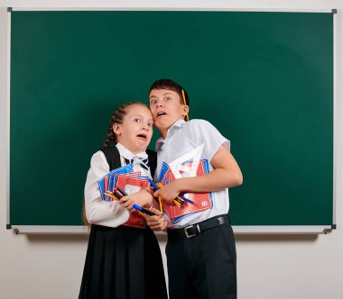 Bir okul çocuğu ve kız öğrenci nin duygusal portresi egzersiz kitapları, kalemler, kalemler ve kara tahta arka plan üzerinde diğer okul malzemeleri ile poz - geri okul ve eğitim kavramı