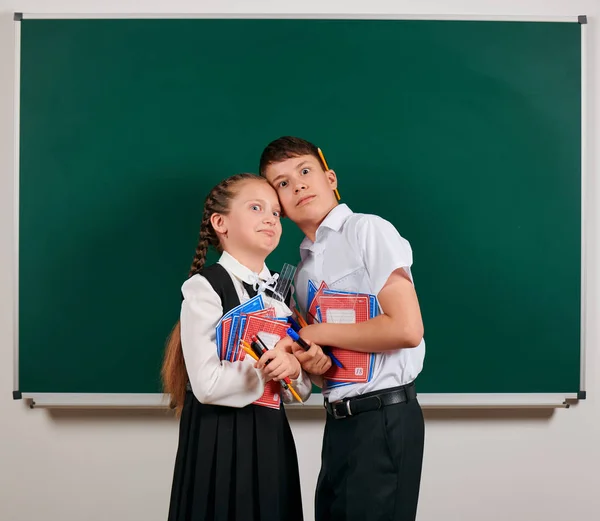 Portrait émotionnel d'un écolier et d'une écolière posant avec des cahiers d'exercices, des stylos, des crayons et d'autres fournitures scolaires sur fond de tableau noir - concept de retour à l'école et d'éducation — Photo