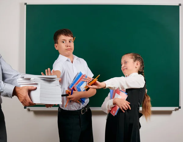 Emotional portrait of a schoolboy and schoolgirl get a lot of books, posing with notebooks, pens, pencils and other school supplies on blackboard background - back to school and education concept — Stock Photo, Image