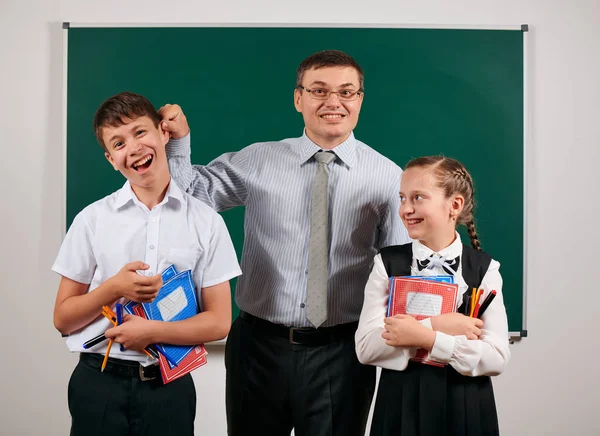 Portrét učitelova ucha, který má špatnou disciplínu a šťastnou školku. Pózové knihy, pera, tužky a další školní potřeby na pozadí tabule — Stock fotografie