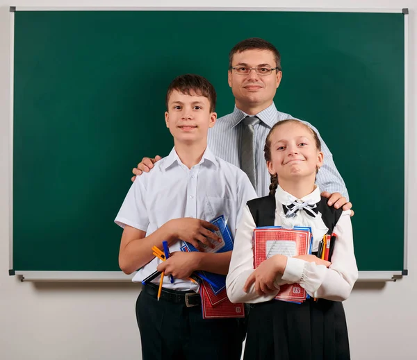 Portrait d'un enseignant, d'un écolier et d'une écolière posant avec des cahiers d'exercices, des stylos, des crayons et d'autres fournitures scolaires sur fond de tableau noir - concept de retour à l'école et d'éducation — Photo