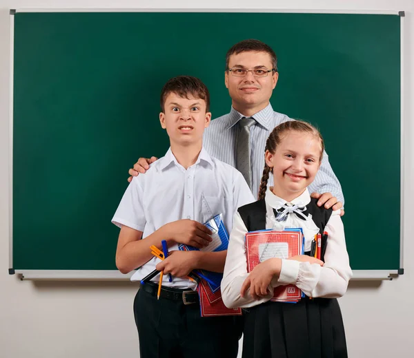 Ritratto di insegnante, scolaro e scolaretta in posa con quaderni, penne, matite e altri materiali scolastici su sfondo lavagna - ritorno a scuola e concetto di istruzione — Foto Stock