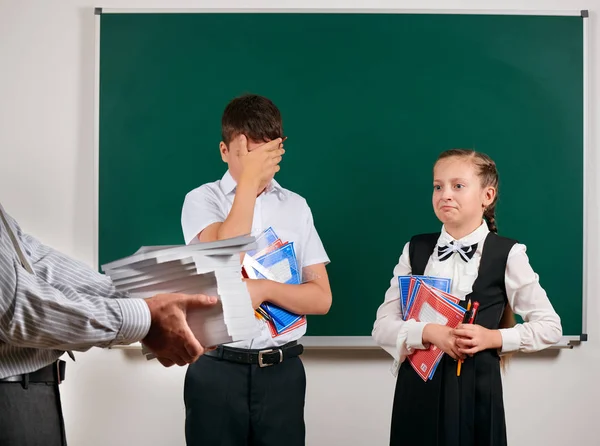 Emotioneel portret van een school jongen en schoolmeisje krijgen veel boeken, poseren met notebooks, pennen, potloden en andere schoolbenodigdheden op Blackboard achtergrond-terug naar school en onderwijsconcept — Stockfoto