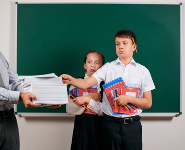 Bir okul çocuğu ve kız öğrenci duygusal portre defterler, kalemler, kalemler ve kara tahta arka plan üzerinde diğer okul malzemeleri ile poz, kitap bir sürü olsun - geri okul ve eğitim kavramı