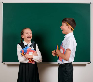 Bir okul çocuğu ve kız öğrenci nin duygusal portresi egzersiz kitapları, kalemler, kalemler ve kara tahta arka plan üzerinde diğer okul malzemeleri ile poz - geri okul ve eğitim kavramı