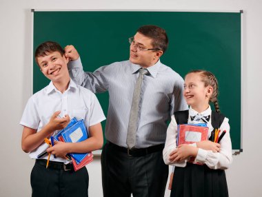 Bir öğretmenin portresi kötü disiplinve mutlu bir kız öğrenci olan okul çocuğunun kulağını kapmak. Kara tahta arka plan üzerinde egzersiz kitapları, kalemler, kalemler ve diğer okul malzemeleri ile poz