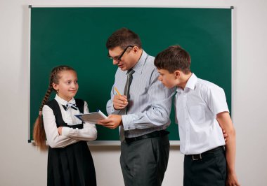 Bir öğretmenin ev ödevi kontrol portresi, okul egzersiz kitapları okuma, eski moda gözlük ile okul çocuğu ve kız öğrenci kara tahta arka plan üzerinde poz - geri okul ve eğitim kavramı