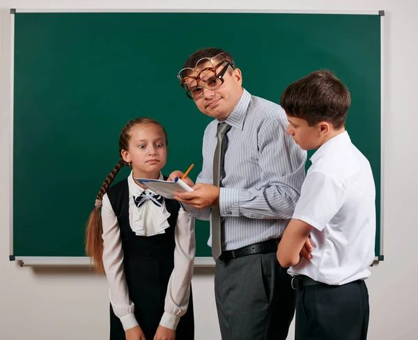 Portrait d'un enseignant vérifiant ses devoirs, lisant des cahiers scolaires, écolier et écolière avec des lunettes à l'ancienne posant sur fond de tableau noir - concept de retour à l "école et d" éducation — Photo