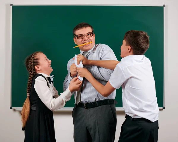 Portrait of a teacher checking homework, reading school exercise books, schoolboy and schoolgirl with old fashioned eyeglasses posing on blackboard background - back to school and education concept — Stock Photo, Image