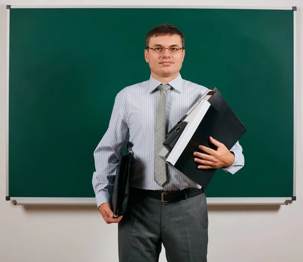 Potret seorang pria yang mengenakan setelan bisnis dengan folder, dokumen dan tas kerja, berpose di latar belakang papan tulis belajar dan konsep pendidikan — Stok Foto