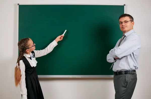 Portrait of a teacher and schoolgirl, posing at blackboard background - back to school and education concept — Stock Photo, Image