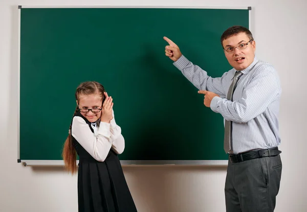 Maestro enojado gritar a la colegiala, posando en el fondo pizarra - volver a la escuela y el concepto de educación — Foto de Stock