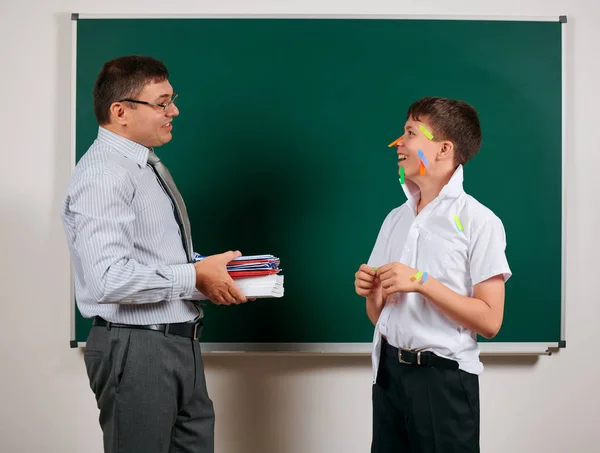 Portrait of a teacher and funny schoolboy with low discipline, poor school performance, posing at blackboard background - back to school and education concept