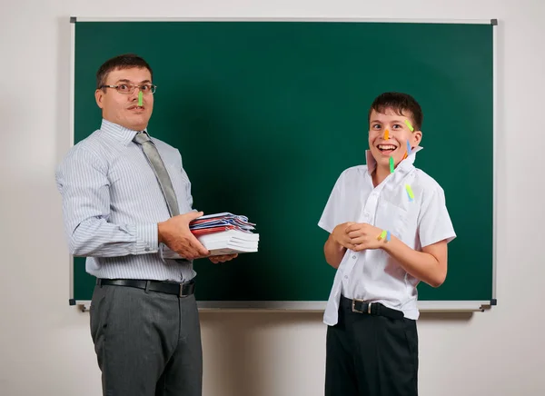 Portrait of a teacher and funny schoolboy with low discipline, poor school performance, posing at blackboard background - back to school and education concept — Stock Photo, Image