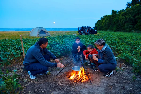 Famiglia in viaggio e in campeggio, crepuscolo, cucina sul fuoco. Bella natura - campo, foresta e luna . — Foto Stock