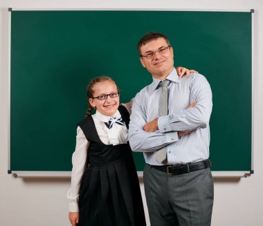 Bir öğretmen ve kız öğrenci portresi, kara tahta arka planda poz - geri okul ve eğitim kavramı