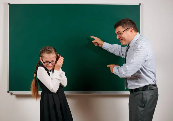 Сердитий вчитель кричить школярці, позує на фоні дошки назад до школи та концепції освіти — стокове фото