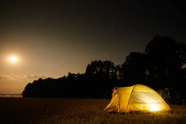 Concept de voyage et de camping - tente de camping la nuit sous un ciel étoilé. Tente éclairée orange et voiture. Belle nature - champ, forêt, plaine. Lune et clair de lune — Photo