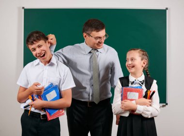 Bir öğretmenin portresi kötü disiplinve mutlu bir kız öğrenci olan okul çocuğunun kulağını kapmak. Kara tahta arka plan üzerinde egzersiz kitapları, kalemler, kalemler ve diğer okul malzemeleri ile poz