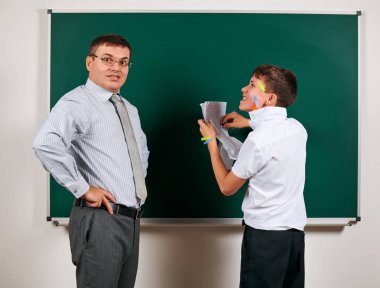 Düşük disiplinli bir öğretmen ve komik bir öğrencinin portresi. Öğrenci çok duygusal, eğlenceli ve çok mutlu, kara tahta arka planda poz - geri okul ve eğitim kavramı