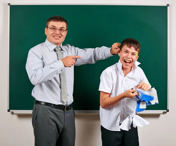Portrait of a teacher catch the ear funny schoolboy with low discipline. Pupil very emotional, having fun and very happy, posing at blackboard background - back to school and education concept — Stock Photo, Image