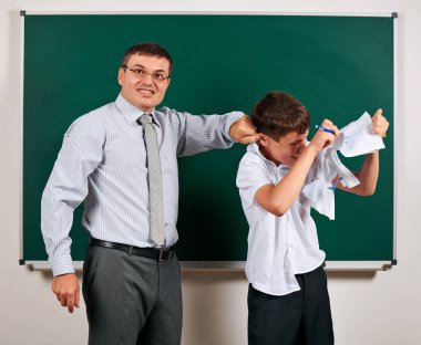 Bir öğretmenin portresi düşük disiplin ile kulak komik öğrenci yakalamak. Öğrenci çok duygusal, eğlenceli ve çok mutlu, kara tahta arka planda poz - geri okul ve eğitim kavramı