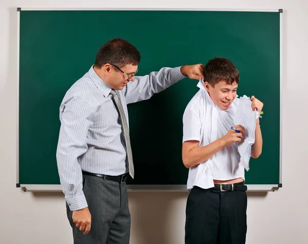Portrait of a teacher catch the ear funny schoolboy with low discipline. Pupil very emotional, having fun and very happy, posing at blackboard background - back to school and education concept — Stock Photo, Image