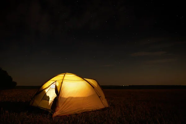 Concetto di viaggio e campeggio - tenda da campeggio di notte sotto un cielo pieno di stelle. Tenda arancione illuminata. Bella natura - campo, foresta, pianura. Luna e chiaro di luna — Foto Stock