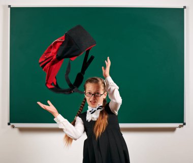 Sırt çantası ve kara tahta arka plan yakınında okul malzemeleri ile oynayan bir kız öğrenci portresi - geri okul ve eğitim kavramı