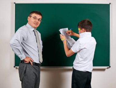 Düşük disiplinli bir öğretmen ve komik bir öğrencinin portresi. Öğrenci çok duygusal, eğlenceli ve çok mutlu, kara tahta arka planda poz - geri okul ve eğitim kavramı