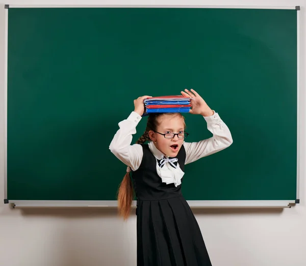 Retrato de una colegiala muy emotiva, estudiante jugando con libros de trabajo y útiles escolares cerca de la pizarra de fondo - volver a la escuela y el concepto de educación — Foto de Stock