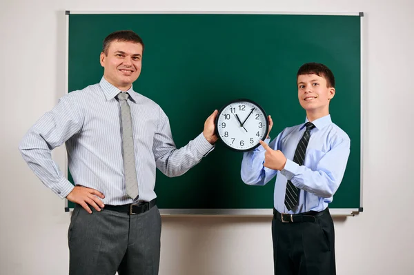 Porträt eines Mannes und eines Jungen in einem Business-Anzug in der Nähe der Tafel Hintergrund, zeigen sie Uhr - Lern- und Bildungskonzept — Stockfoto