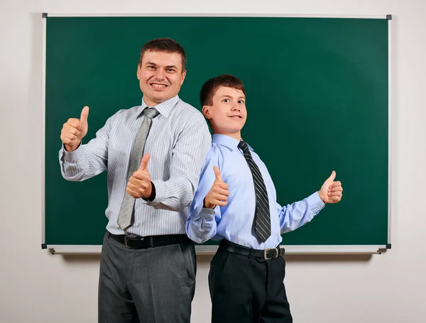 Portrait of a man and boy dressed in a business suits near blackboard background, they show best gesture - learning and education concept — Stock Photo, Image