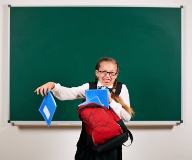 Sırt çantası ve kara tahta arka plan yakınında okul malzemeleri ile oynayan bir kız öğrenci portresi - geri okul ve eğitim kavramı