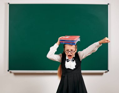 Çok duygusal bir kız öğrenci portresi, çalışma kitapları ve kara tahta arka plan yakın okul malzemeleri ile oynayan öğrenci - geri okul ve eğitim kavramı