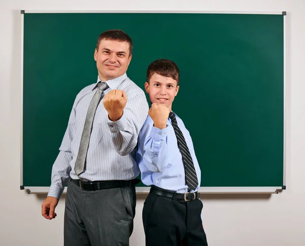 Portrait of a man and boy dressed in a business suits near blackboard background, they show fists - learning and education concept — Stock Photo, Image
