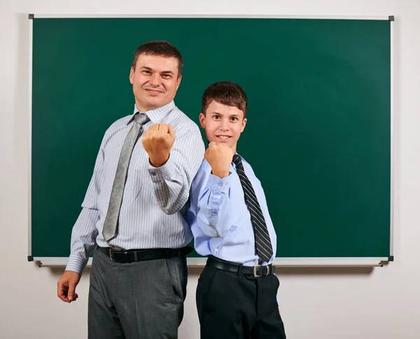 Porträt eines Mannes und eines Jungen im Business-Anzug in der Nähe der Tafel, sie zeigen Fäuste - Lern- und Bildungskonzept Stockfoto