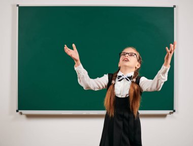 Sırt çantası ve kara tahta arka plan yakınında okul malzemeleri ile oynayan bir kız öğrenci portresi - geri okul ve eğitim kavramı