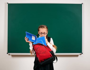 Sırt çantası ve kara tahta arka plan yakın okul malzemeleri ile bir kız öğrenci portresi - geri okul ve eğitim kavramı